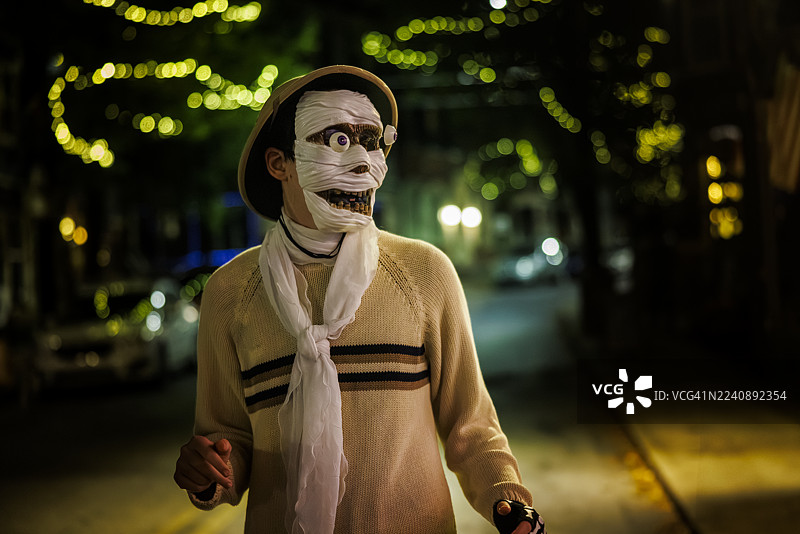 创意打扮的年轻自闭症患者戴着精致的木乃伊面具和帽子，在充满节日气氛的街灯下庆祝万圣节之夜。图片素材
