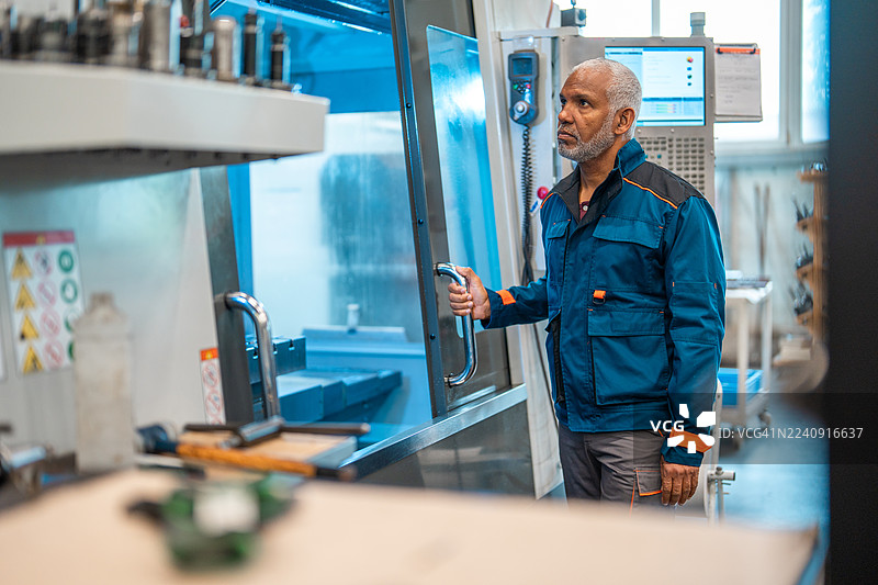 车间里，一位成熟的西班牙裔技术人员正在操作数控机床。图片素材