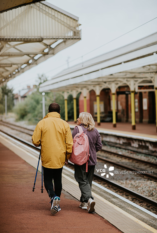 一对年长的夫妇在英国的火车站台上行走，他们身着休闲户外服装。图片素材
