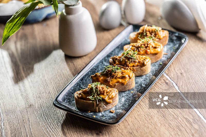 一排四个开胃菜，小吃，上面淋着奶油酱，并饰以新鲜的豆芽和酥脆的撒料。这些小点心以碎牛肉里脊酱搭配融化的切达奶酪制成，风味浓郁。图片素材