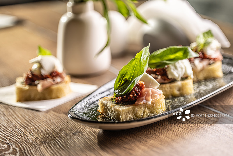 扁长形餐盘上摆放着撒有太阳番茄干、意大利熏火腿和罗勒叶的佛卡夏面包片，作为餐厅开胃菜。图片素材
