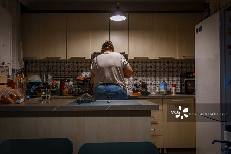 Woman cooking in kitchen at home during evening图片素材