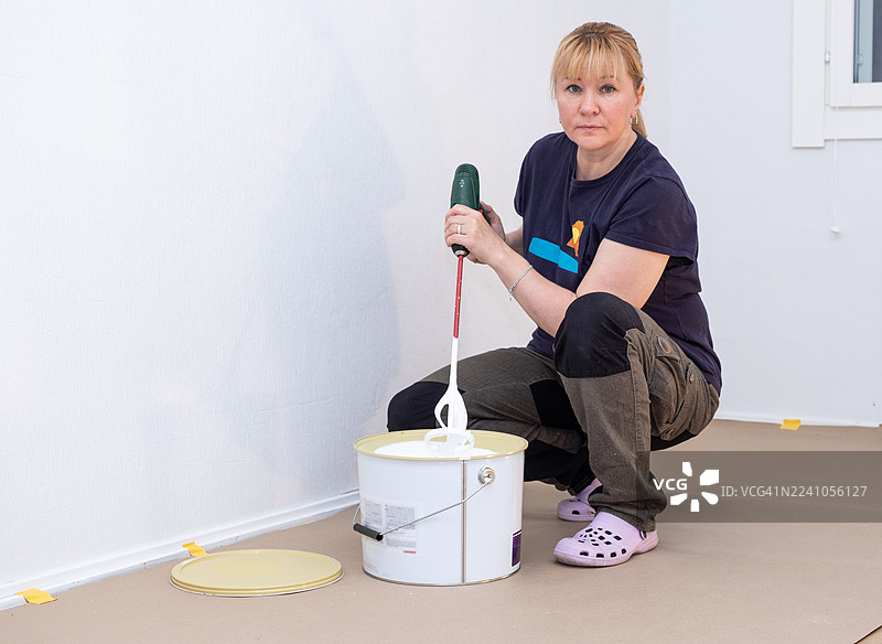 一位40岁的白人女画家正在用无绳电钻和搅拌器搅拌油漆。图片素材