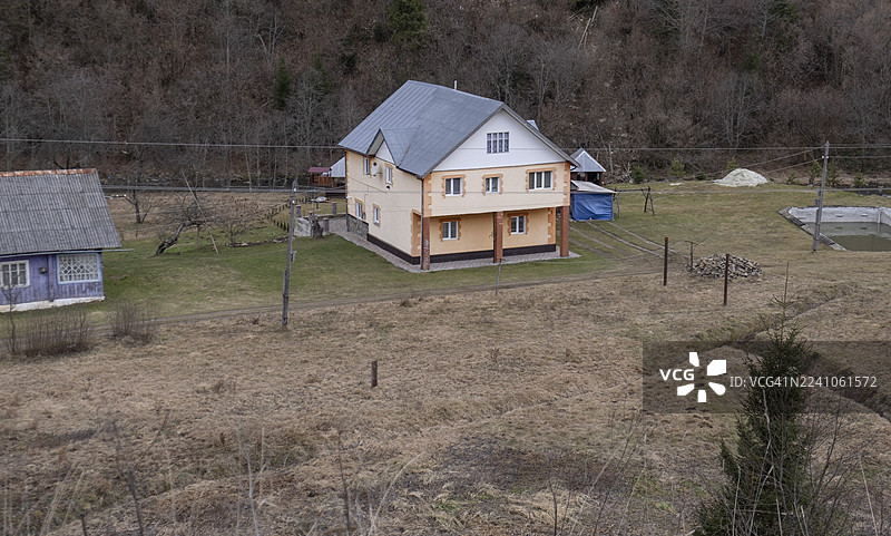 喀尔巴阡山区东欧乡村，传统与现代房屋并存，有电线杆，下方是初春时节休眠的山脉和一片荒草丛生的田野图片素材