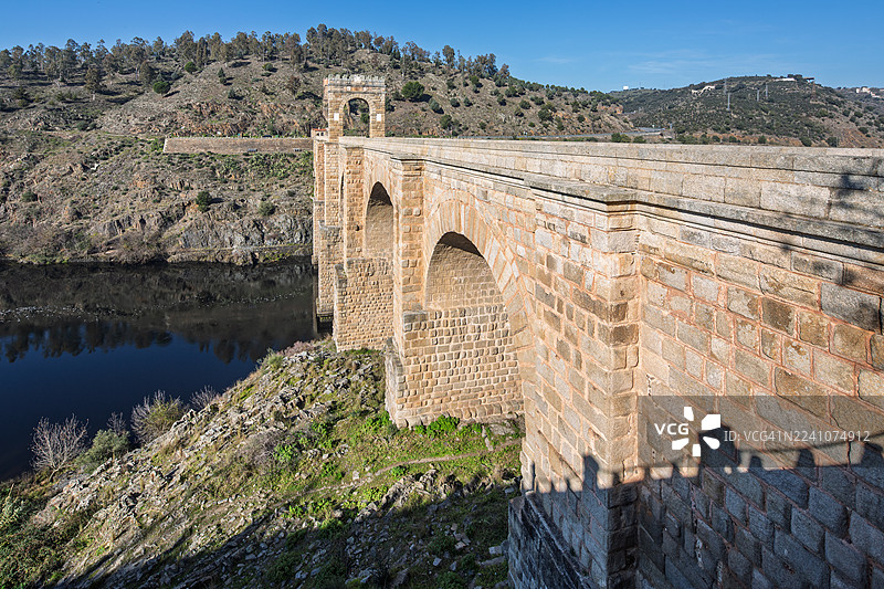 西班牙，古罗马拱桥横跨河流，背景为丘陵地貌，天空湛蓝图片素材