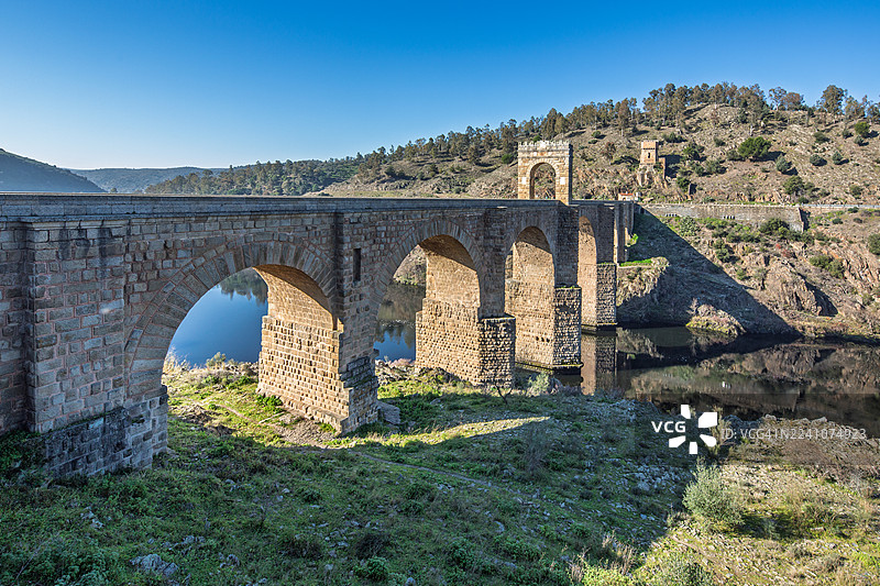 古罗马拱桥横跨河流，背景是晴朗的蓝天和乡村风光，西班牙图片素材