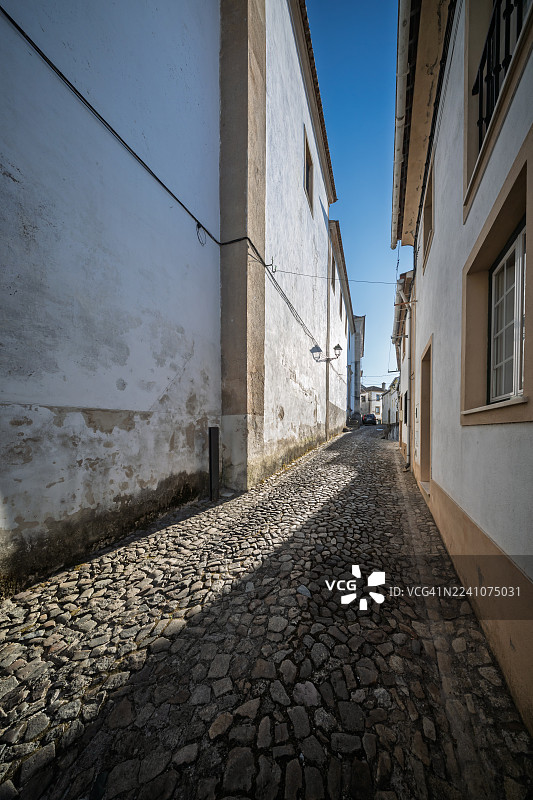 阳光下的城市，一条鹅卵石小巷蜿蜒穿过历史建筑，营造出宁静和被遗忘的小径之感，葡萄牙，卡斯特洛-德维德，市中心图片素材
