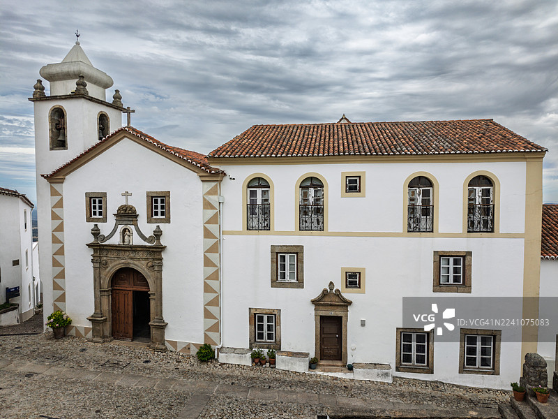 低角度拍摄的葡萄牙历史悠久的白色教堂，带有钟楼和瓷砖屋顶，背景是多云的天空，展示了传统的建筑风格。地点：卡斯特洛-德维德市中心。图片素材