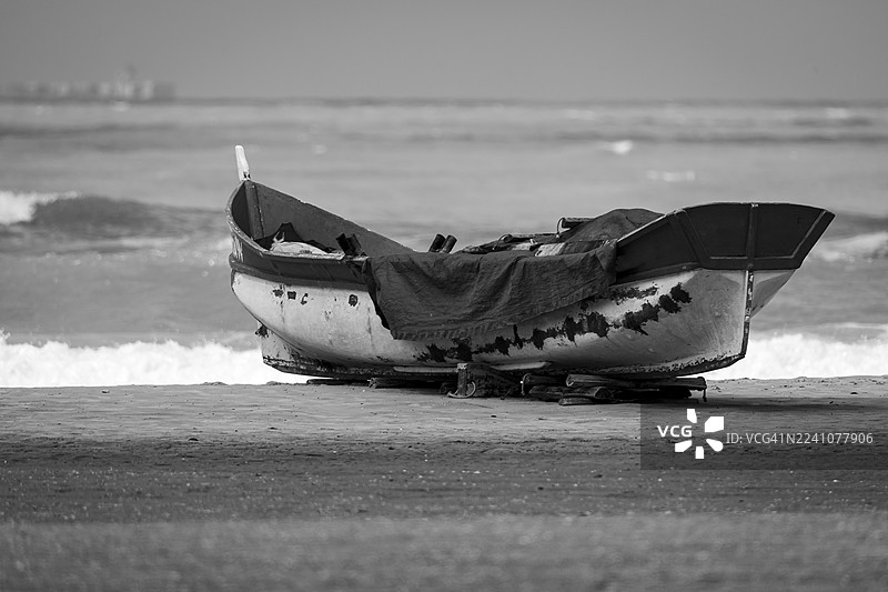 黑白照片：一艘旧渔船停靠在沙滩上，背景是海浪。图片素材