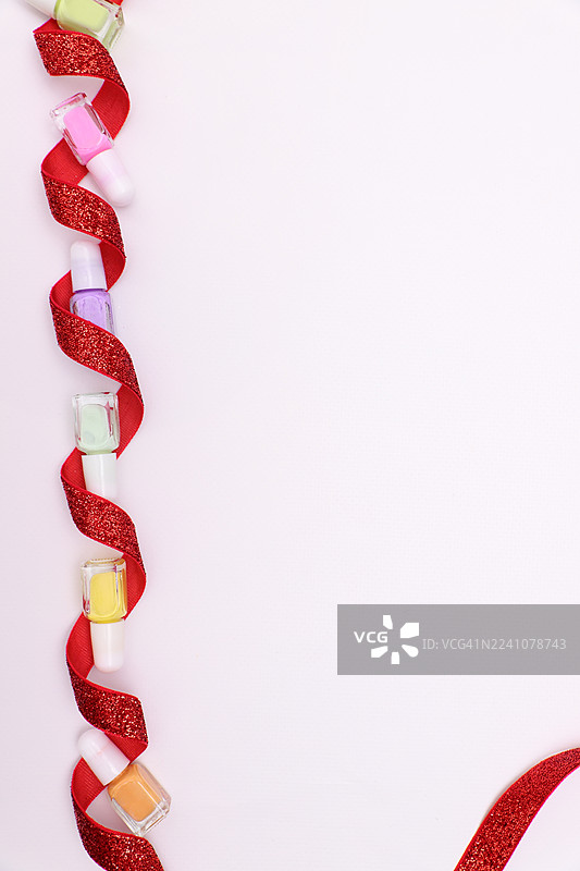 纯净的白色背景上，鲜艳的指甲油瓶与闪亮的红色丝带交织在一起，营造出节日般的缤纷景象。图片素材