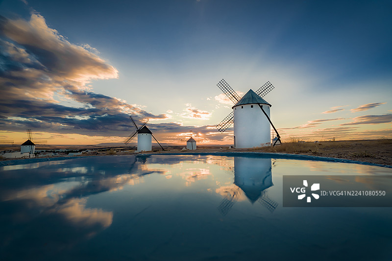 西班牙拉曼恰坎波德克里普塔纳的传统风车在戏剧性的日落时分倒映在水中图片素材