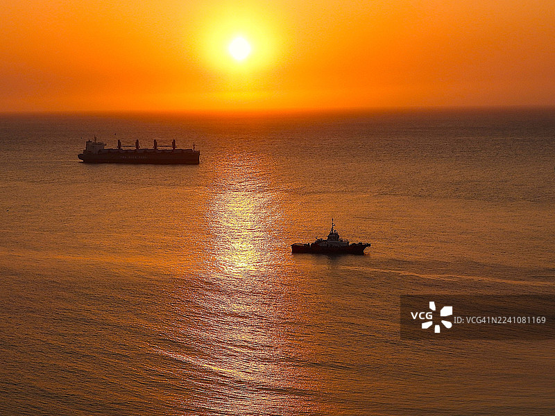 日落时海上货船和拖船的剪影，天空呈现出鲜艳的橙色，哥伦比亚阿拉乌卡，圣玛尔塔图片素材