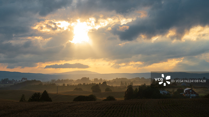 挪威乌伦萨克，夕阳下的乡村景色，阳光穿透云层，薄雾笼罩田野图片素材