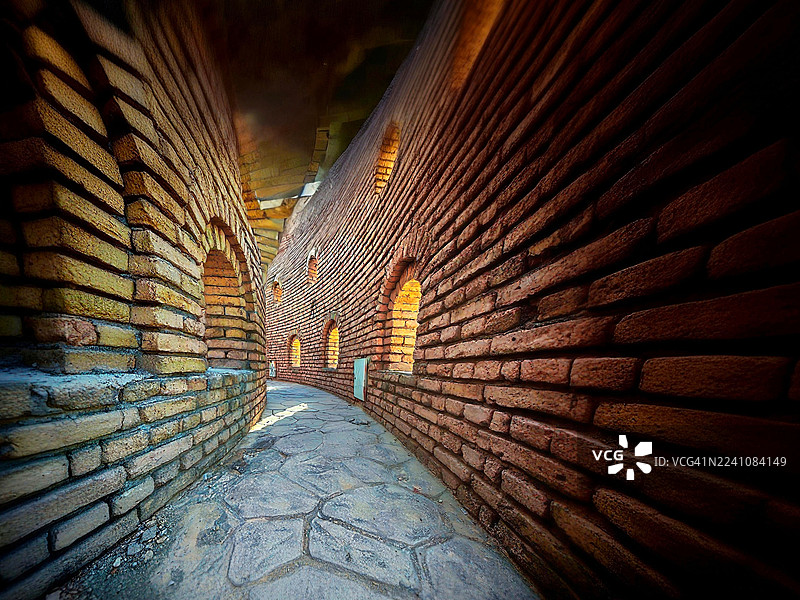 一条狭窄弯曲的砖砌小径，拱形窗户被光线照亮，营造出神秘和古老历史的氛围，伊拉克埃尔比勒图片素材