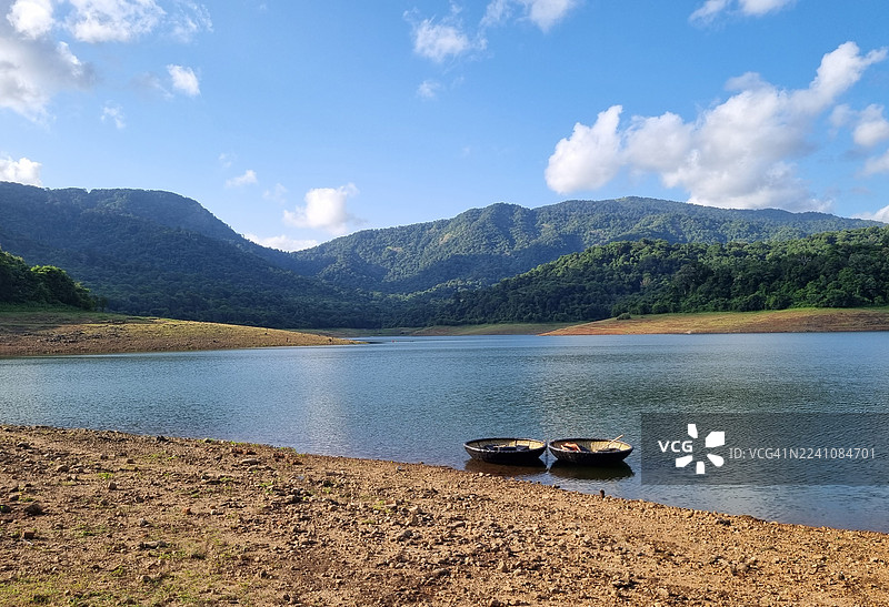 宁静的湖面上漂浮着两艘小船，背景是郁郁葱葱的绿色山峦，天空湛蓝明亮。图片素材