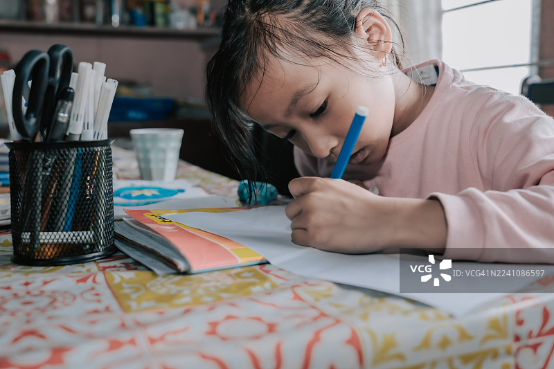 一个小女孩在家专注地在纸上用蓝色记号笔画画图片素材