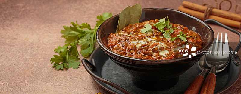 美味的印度扁豆玛卡尼或奶油扁豆咖喱，配以香草，盛在碗里，放在乡村风格的桌子上，旁边还有香料。图片素材