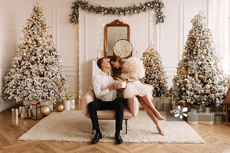 一对情侣身着优雅服饰，在豪华住宅中装饰圣诞树并交换礼物。图片素材