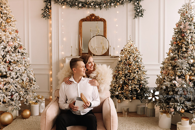 浪漫情侣身着优雅服饰在豪华住宅中装饰圣诞树并交换礼物图片素材