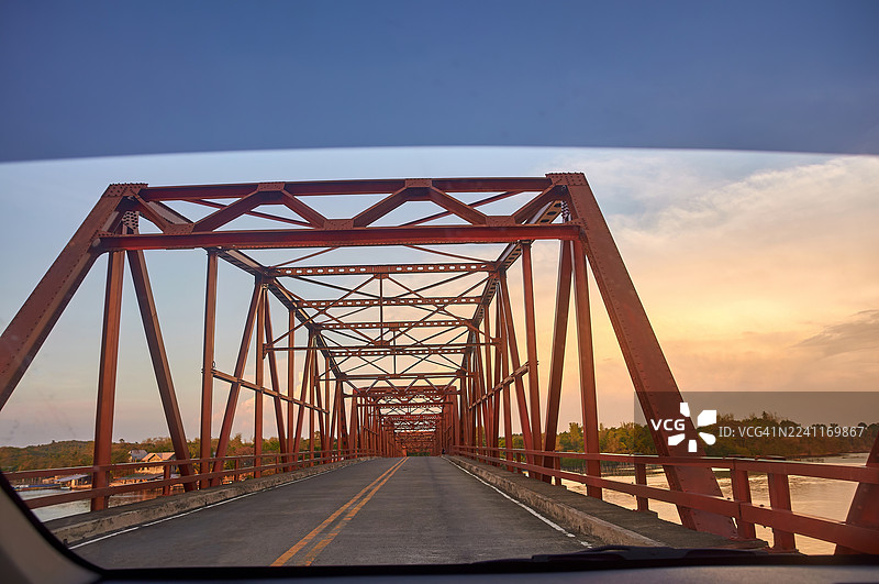 从车内望去，一座红色的金属桁架桥在暖色调的天空下闪耀。图片素材