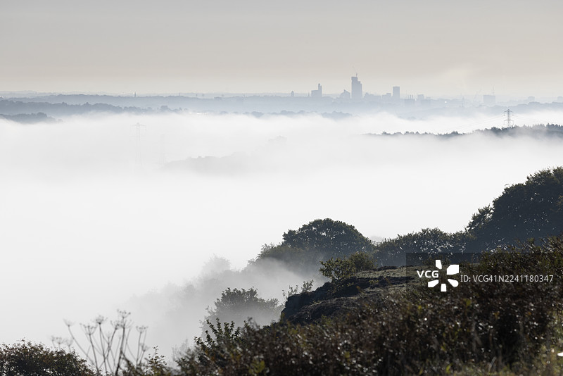英国西约克郡，从拜尔登莫尔山向利兹市中心摩天大楼方向的雾气笼罩的景象图片素材