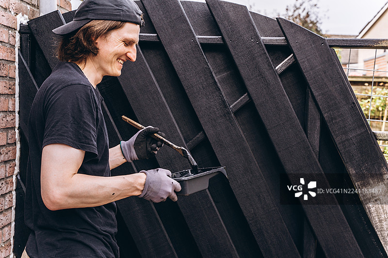 一个年轻男子在户外粉刷木栅栏图片素材