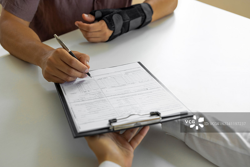 一名手臂骨折的匿名男子正在填写表格图片素材