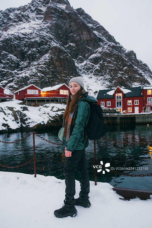 一位英俊的女士在渔村散步，背景是罗弗敦的红色罗布尔小屋。图片素材