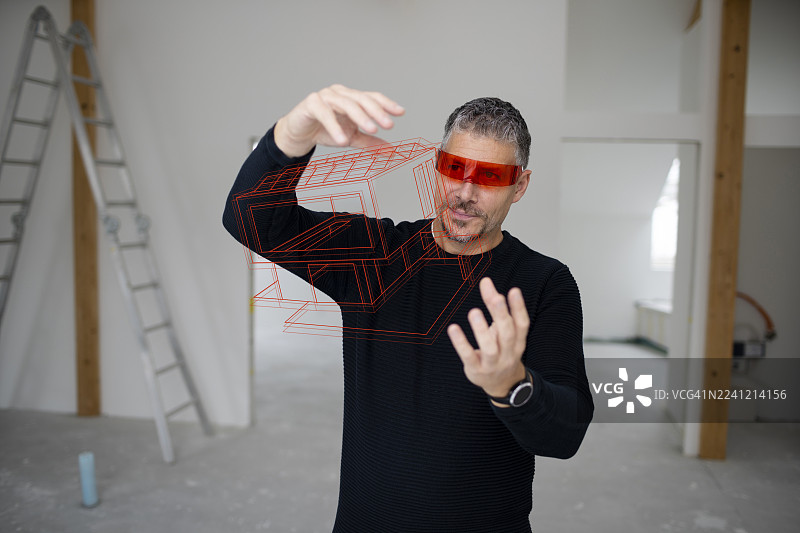 身穿红色虚拟现实模拟器的建筑师在建筑工地上检查房屋模型图片素材