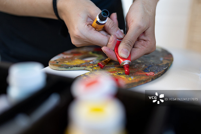 特写：双手将红色颜料挤到调色板上图片素材