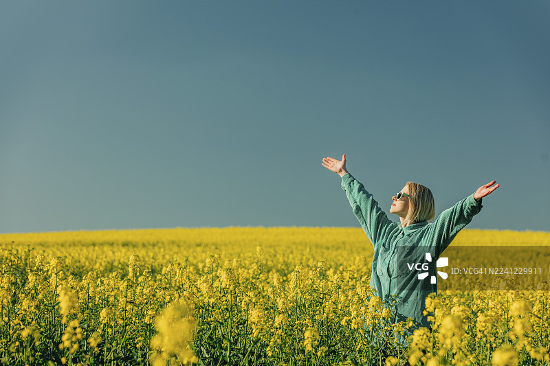女子张开双臂，站在油菜花田中图片素材