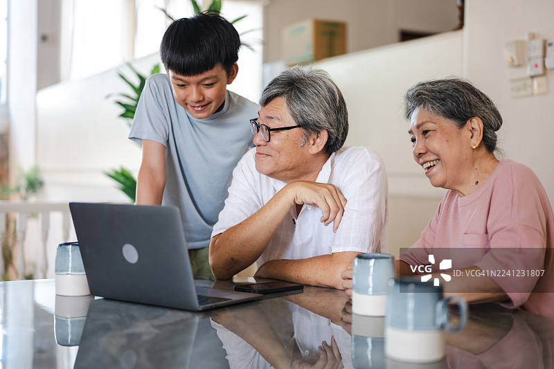 一个中国小男孩在教他的祖父学习新的电脑技术。这位年迈的祖父在家学习使用电脑。图片素材