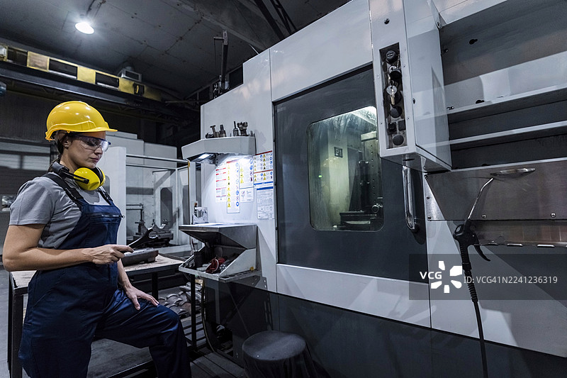 现代工厂里，一名维护工程师手持扳手站在数控机床旁图片素材