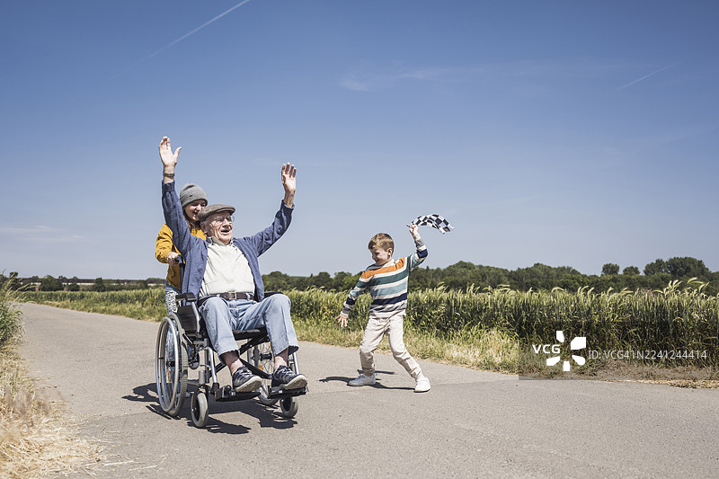 晴天，男孩举着格子旗，一位老人坐在轮椅上图片素材
