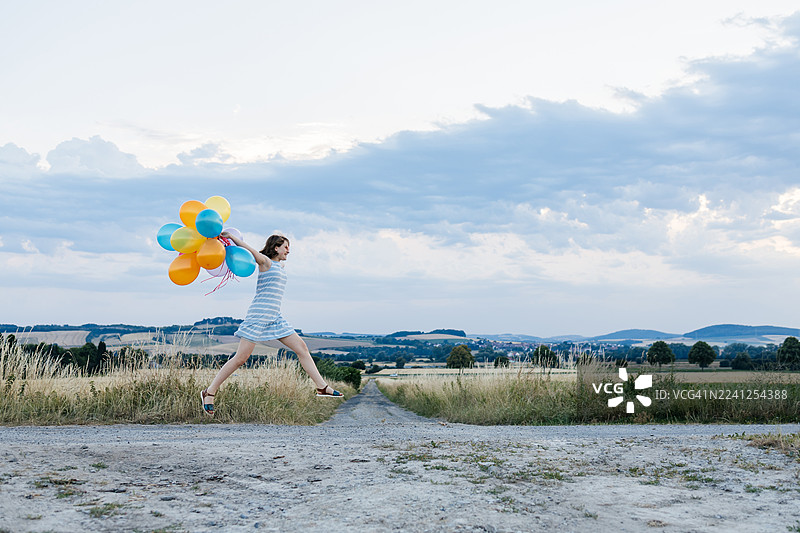 身穿心形太阳镜的女孩在夏日草地上带着气球跳跃图片素材