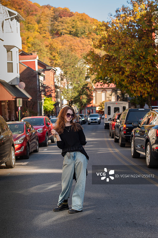 秋叶满坡，长发年轻女子在宾夕法尼亚州历史悠久的小镇街道上摆姿势。图片素材