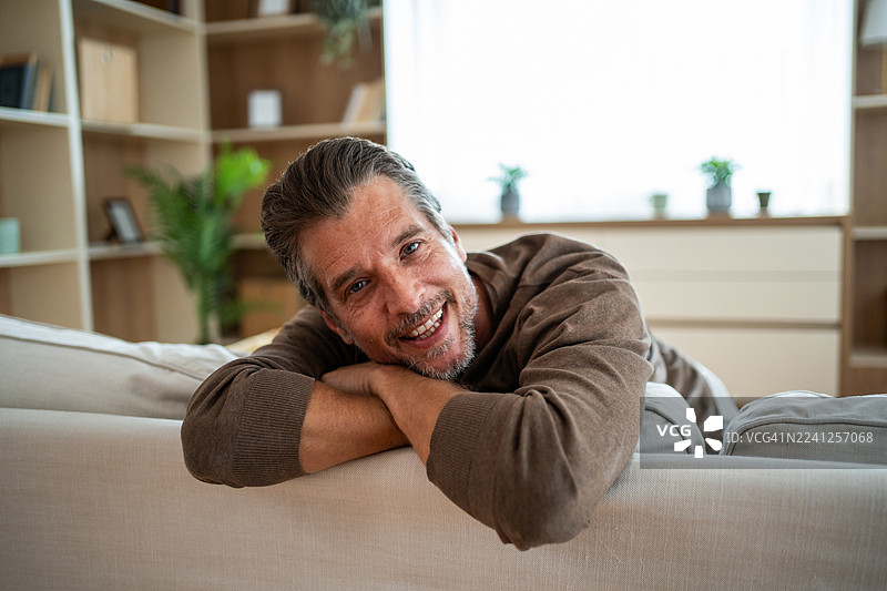男人放松地坐在沙发上，微笑着看向镜头图片素材