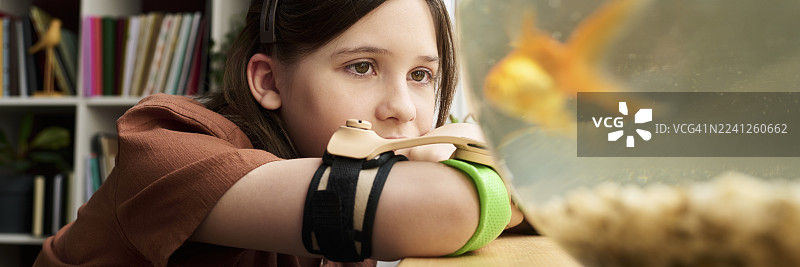 一个装有假肢的孩子在家沉思地看着金鱼图片素材