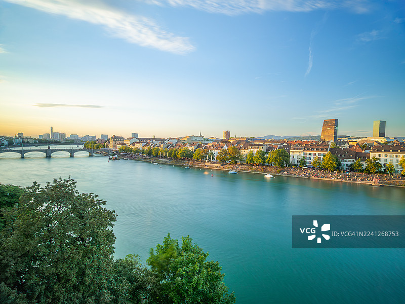 夏季日落时分，瑞士巴塞尔城市巴塞尔市克莱因巴塞尔区和莱茵河码头的长曝光景观，岸边是熙熙攘攘的滨河大道，还有一座古老的拱桥——米特勒布吕克（中桥）。图片素材
