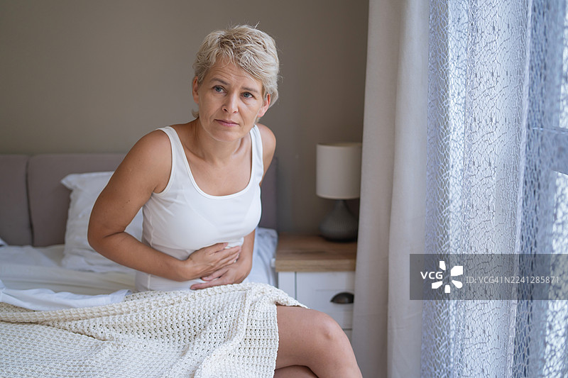 一位忧心忡忡的女性在宁静的卧室里捂着肚子图片素材