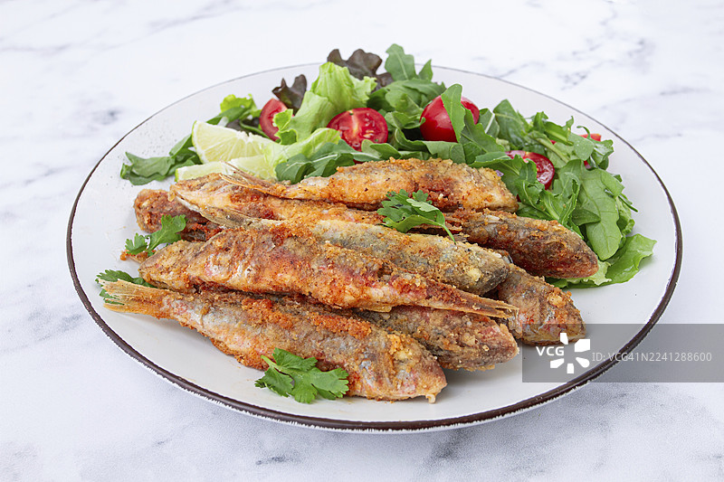 炸至酥脆的鲻鱼，配上新鲜沙拉，盘子里放着青柠，无人像图片素材