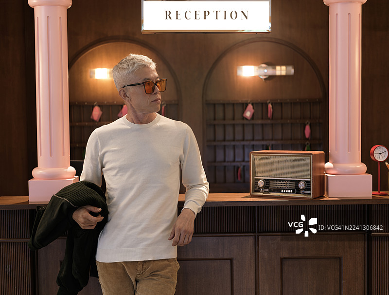 一位时尚的亚洲中年男性站在装饰复古的酒店接待台前。图片素材