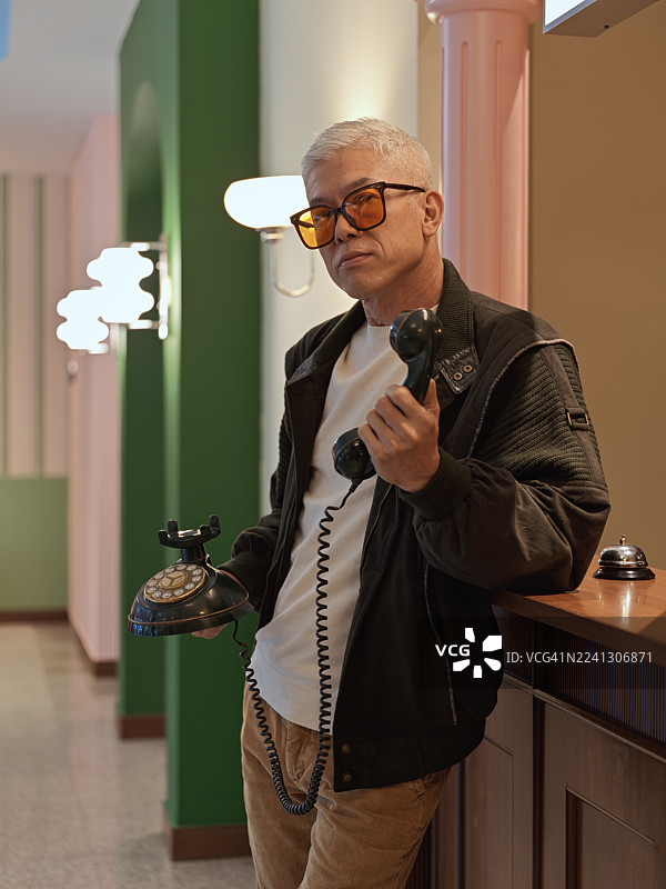 一位年长的中国男士在酒店前台拿着老式电话图片素材