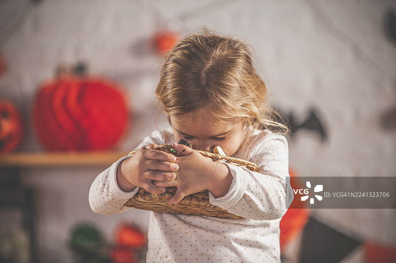 可爱的小女孩脸贴着编织篮子，背景是万圣节南瓜。图片素材
