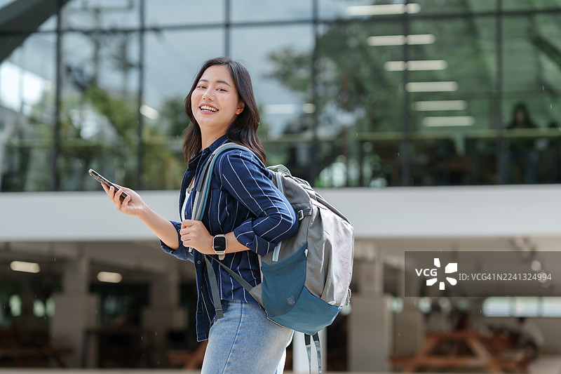 年轻的大学生在校园里边走边玩手机。图片素材