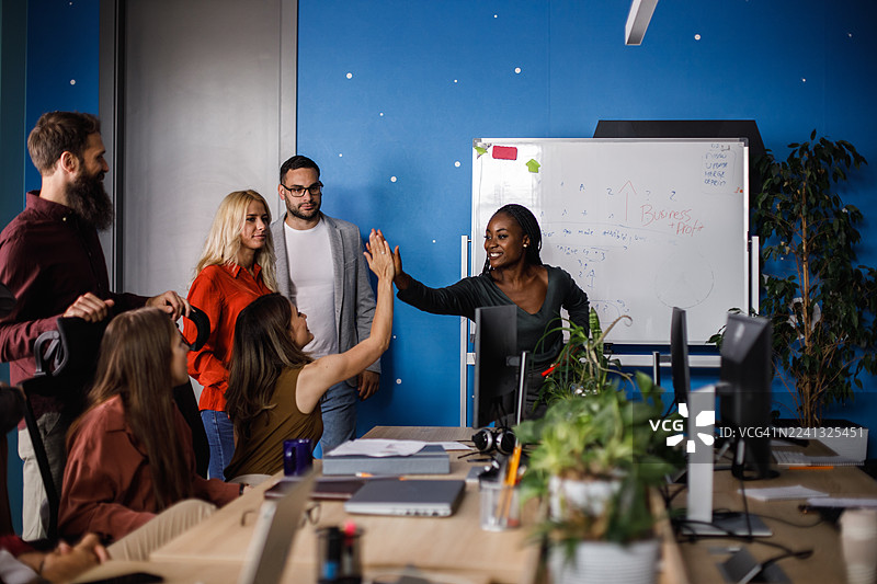 多元化团队在明亮的蓝色办公室的一次头脑风暴会议后击掌庆祝图片素材