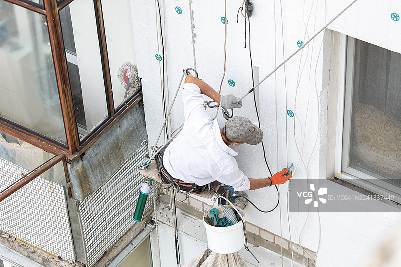 一名建筑工人在高处用聚苯乙烯板为建筑物外墙保温。图片素材