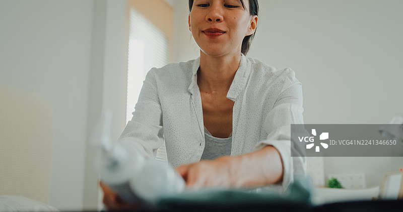 近距离拍摄一名年轻亚洲女性在家卧室的床上打包行李箱，为轻松的夏季度假旅行准备衣物和个人物品。图片素材