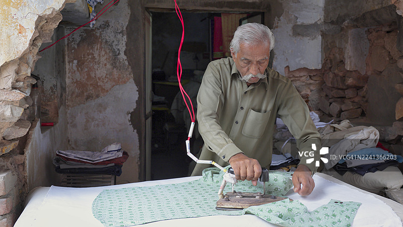 一位年长的印度男性在熨烫衣服图片素材