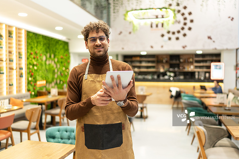 男餐厅老板微笑着用平板电脑经营他的小生意图片素材